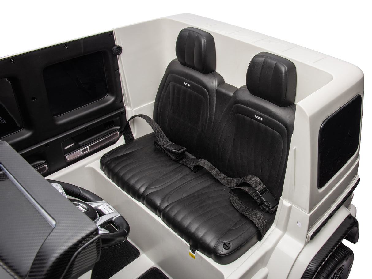 The White 2x24V/4WD Platinum XXL Mercedes G63 Ride On Truck features a luxurious interior with two black leather seats with seatbelts, a steering wheel, and a sleek dashboard, reminiscent of an electric golf cart.