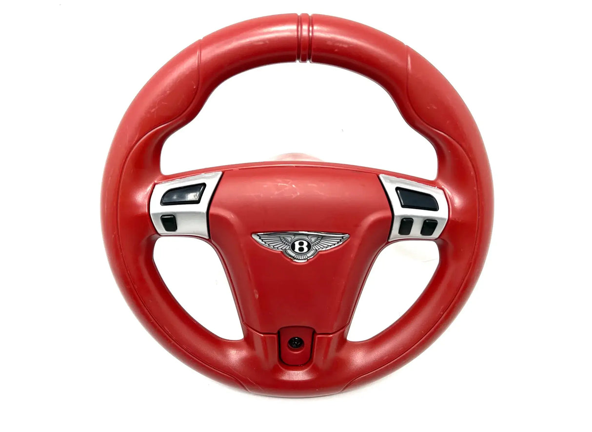 The 12V Bentley Sport GT Steering Wheel is a red toy with ergonomic grips and the Bentley logo at the center. It features black and silver buttons, ideal for a childs ride-on car. Available exclusively at KidsVIPOnline as a final sale.