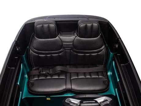 The image shows the interior of the Green Metallic 24V Kids Range Rover, a luxurious ride-on SUV, with two sleek black leather seats featuring prominent stitching and a textured pattern. A seatbelt is visible, and the surrounding area boasts a glossy finish that mirrors high-end convertibles.