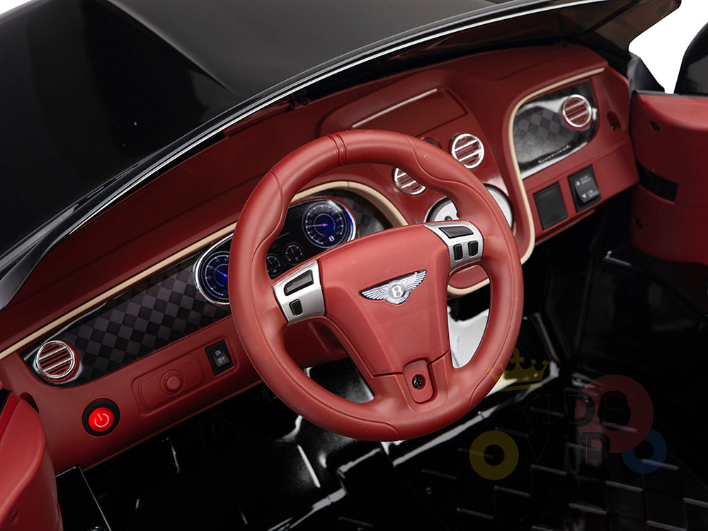 The product is a Black 12V Bentley GTC Kids Licensed Ride On Car, featuring rubber wheels and a remote. Its sophisticated design highlights luxurious elements like circular air vents, emblem details on a red steering wheel, blue-lit dials, and sleek control buttons for an opulent charm.