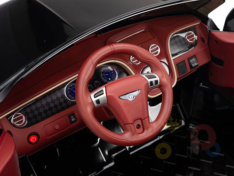 The product is a Black 12V Bentley GTC Kids Licensed Ride On Car, featuring rubber wheels and a remote. Its sophisticated design highlights luxurious elements like circular air vents, emblem details on a red steering wheel, blue-lit dials, and sleek control buttons for an opulent charm.