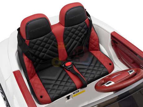 Close-up of the White 12V Bentley GTC Kids Licensed Ride On Cars interior, showcasing two black and red quilted leather seats with seatbelts, a matching steering wheel, and dashboard controls. This miniature version mirrors the craftsmanship of a real Bentley.