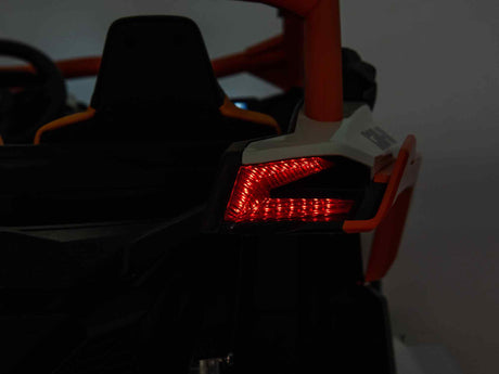 Close-up of the rear section of the Red 2x24V/4WD Official Can-Am Maverick Ride on Buggy, LX Performance, highlighting a distinct red taillight in a sleek angular design. The dark bodywork with orange and white accents enhances its sporty 2-seater aesthetic.