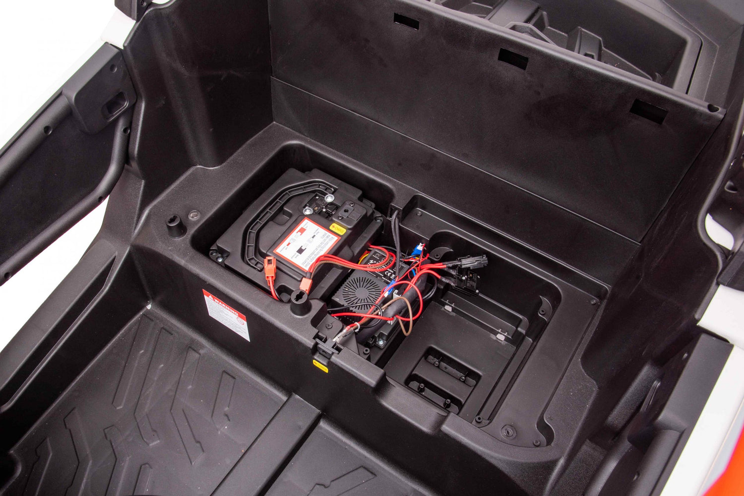 An open compartment in the Yellow 2x24V/4WD Official Can-Am Maverick Ride on Buggy, LX Performance Edition reveals a battery with connected red and black cables. The black surrounding area has molded plastic sections and a textured floor, enhancing its rugged design.
