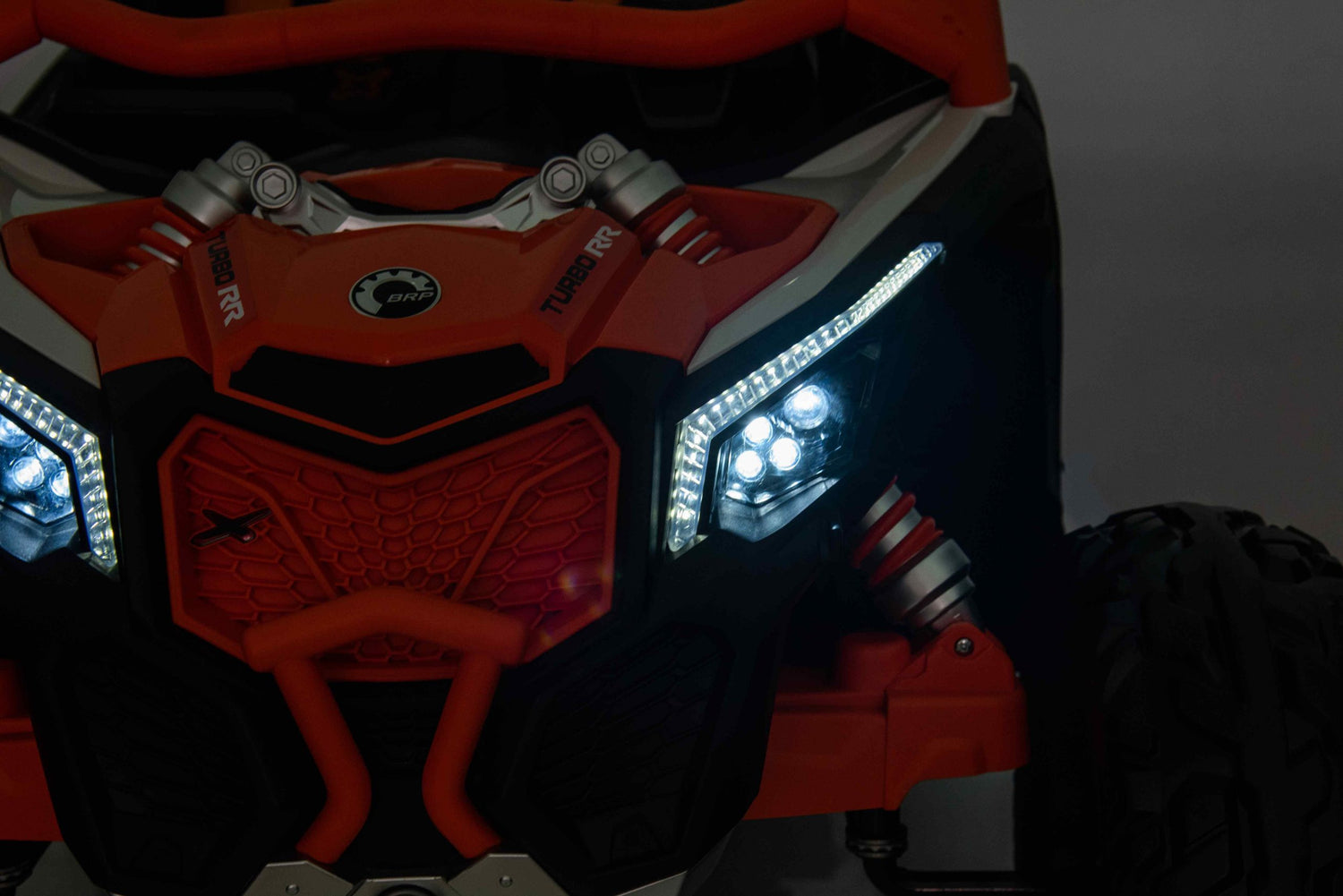 A close-up of the Rose 2x24V/4WD Official Can-Am Maverick Ride on Buggy, LX Performance highlights its rugged grille, LED headlights, and robust suspension. Predominantly orange and black, the LX Performance Edition logo on the hood underscores its adventurous spirit.