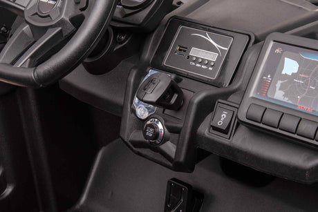The Rose 2x24V/4WD Official Can-Am Maverick Ride-on Buggy, LX Performance Edition, showcases a sleek dashboard with a start/stop button, digital temperature display, and USB port. The steering wheel is visible on the left while a dynamic map screen enhances the right sides luxury.