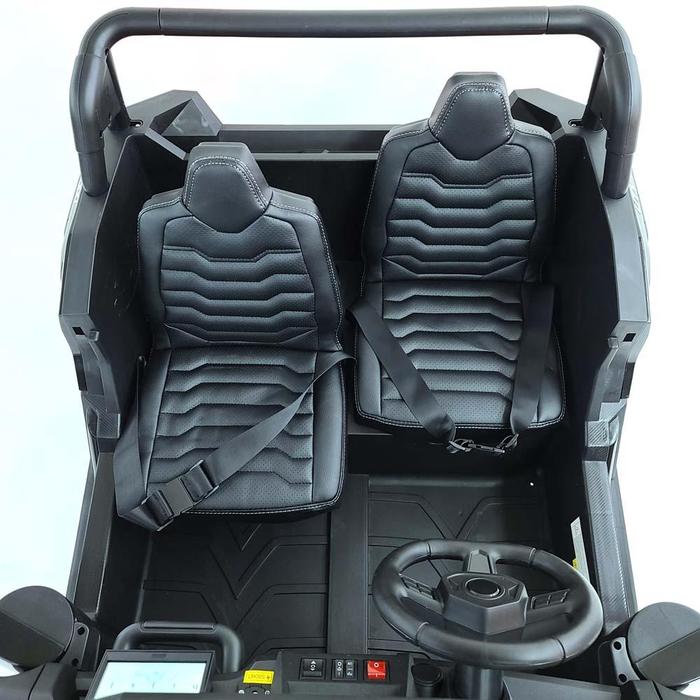 The interior of the White 24V/180W XXL Big Kids Blade XR Ride on Buggy features two black, cushioned seats with hexagonal patterns and seatbelts. It has a dashboard with a small steering wheel, buttons, and a display, while inflatable rubber tires ensure smooth rides ahead.