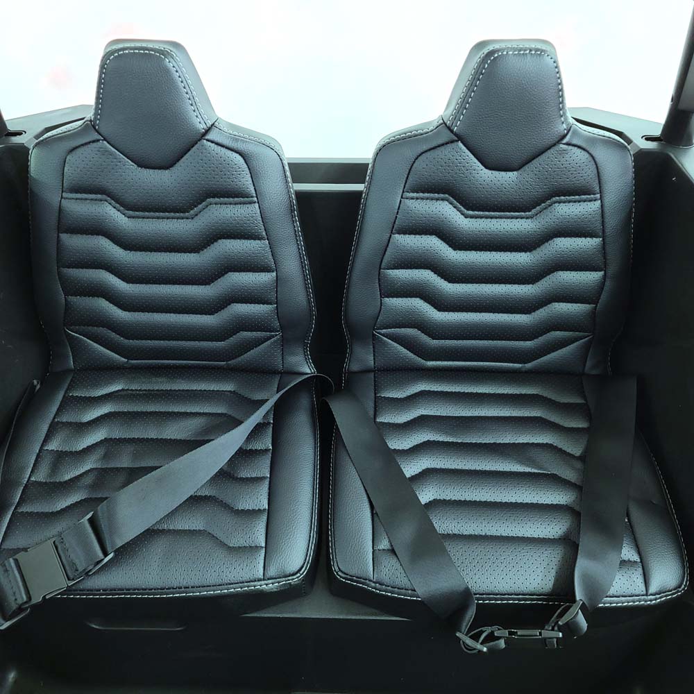 A close-up of the White 24V/180W XXL Big Kids Blade XR Ride on Buggy shows car seats with black leather upholstery and white stitching. The design has horizontal ridges, and both seats feature black seat belts, showcasing the premium craftsmanship of this buggys interior.