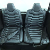 A close-up of the White 24V/180W XXL Big Kids Blade XR Ride on Buggy shows car seats with black leather upholstery and white stitching. The design has horizontal ridges, and both seats feature black seat belts, showcasing the premium craftsmanship of this buggys interior.