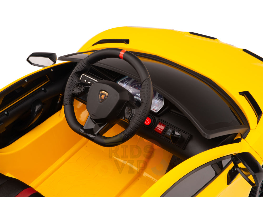 The image features a close-up of the Yellow 12V Lamborghini SVJ Sport Kids Licensed 1 Seater Ride On Cars interior, highlighting a logo-adorned black steering wheel, dashboard with gauges, and side mirror. The sporty design emulates a luxury Lamborghini SVJ car.