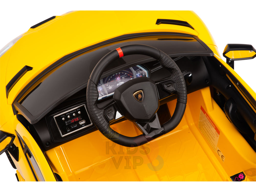 Close-up of the interior of a Yellow 12V Lamborghini SVJ Sport Kids Ride-On. Features include a black steering wheel with a red stripe, digital dashboard, side mirror, and USB infotainment system. This licensed model resembles the sleek design of a luxury sports car.