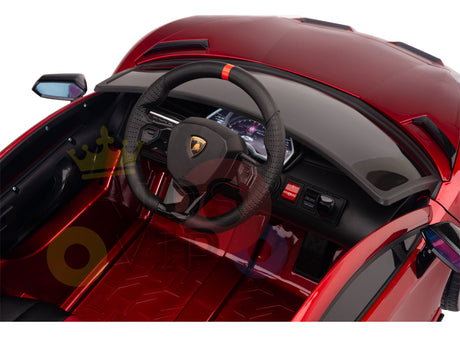 Interior view of a luxury Lamborghini Ride On Car with a black steering wheel featuring red detailing, buttons and gauges on the dashboard, and black seats. The Burgundy Red 12V Lamborghini SVJ Sport boasts two side mirrors and offers an exciting remote control experience for kids.