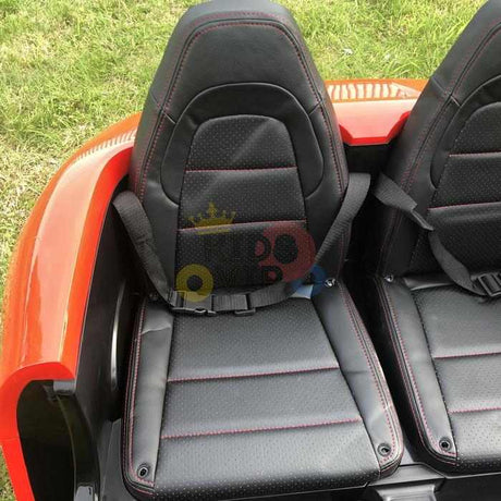 Two black leather car seats with red stitching and seat belts are side by side in an Orange 24V XXL SuperSport Big Kids Ride On Car. Its partially visible exterior contrasts with green grass, hinting at the power of its 180W brushless motor.