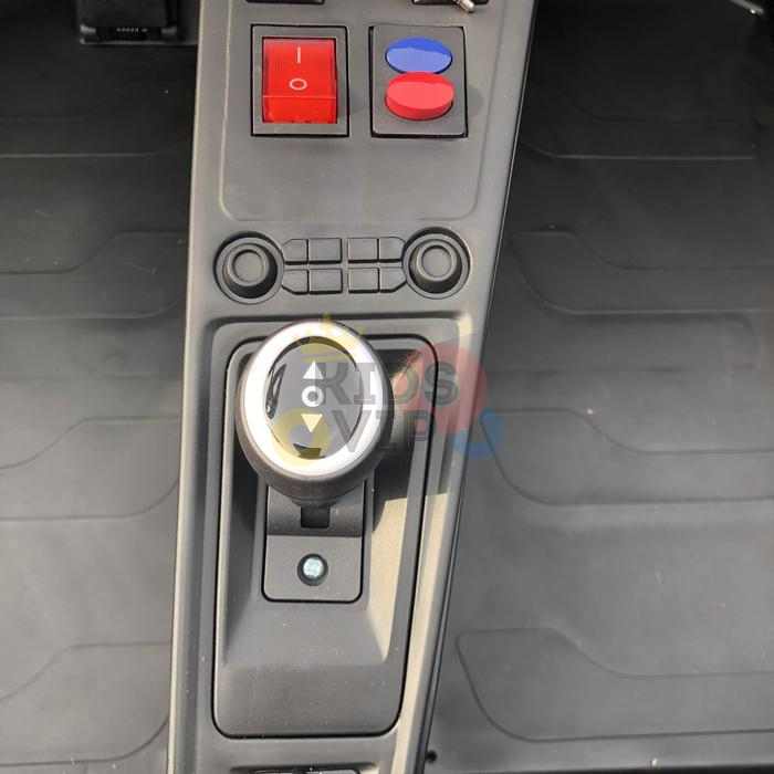 Close-up of the gear shift and dashboard in the Orange 24V XXL SuperSport Big Kids Ride On Car, featuring a round gear knob, two large red buttons, a blue button, and an efficient 180W Brushless Motor within a minimalistic dark interior.