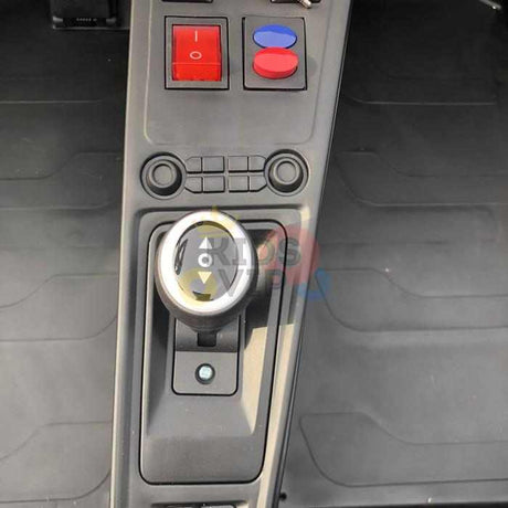 Close-up of the gear shift and dashboard in the Orange 24V XXL SuperSport Big Kids Ride On Car, featuring a round gear knob, two large red buttons, a blue button, and an efficient 180W Brushless Motor within a minimalistic dark interior.