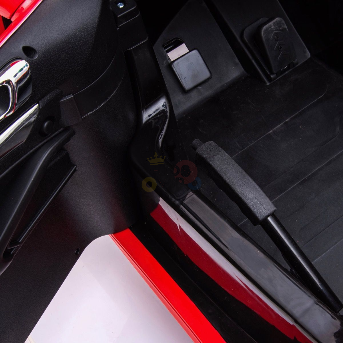 View of an open Red 24V XXL SuperSport Big Kids Ride On Car door, showcasing the pedal area beside the cars vibrant red frame. The floor features black mats, and a sleek dashboard is partially visible.