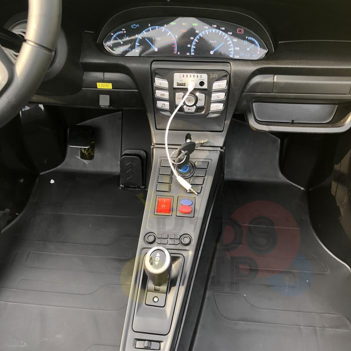 Close-up view of the Metallic Blue 24V XXL SuperSport Cars dashboard and center console, showcasing Eco Leather Seats. Includes a speedometer, buttons, switches, and a charging cable in use. The steering wheel is partly visible on the left.