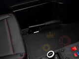 Close-up of the White 24V XXL SuperSport Ride On Car interior featuring a black grip handbrake next to a black padded seat with red stitching; floor has a rubber mat and console buttons are partially visible.