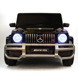 Front view of the Black 24V 2 Seats 4x4 Official Mercedes Benz G63 Complete Edition Kids Ride On Car, featuring illuminated headlights, an AMG logo on the grille, and a silver bumper guard on a white background. Ready to showcase its battery-powered system.
