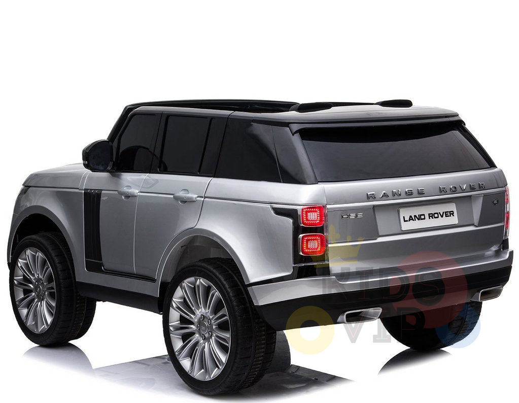 A silver 24V Complete Silver Edition 2 Seats Range Rover Kids Ride On Car with RC, MP4 is parked, shown from the rear-left angle. It features tinted windows, sleek curves, and distinctive rear lights. The iconic Range Rover and Land Rover badges are prominently visible on the back.