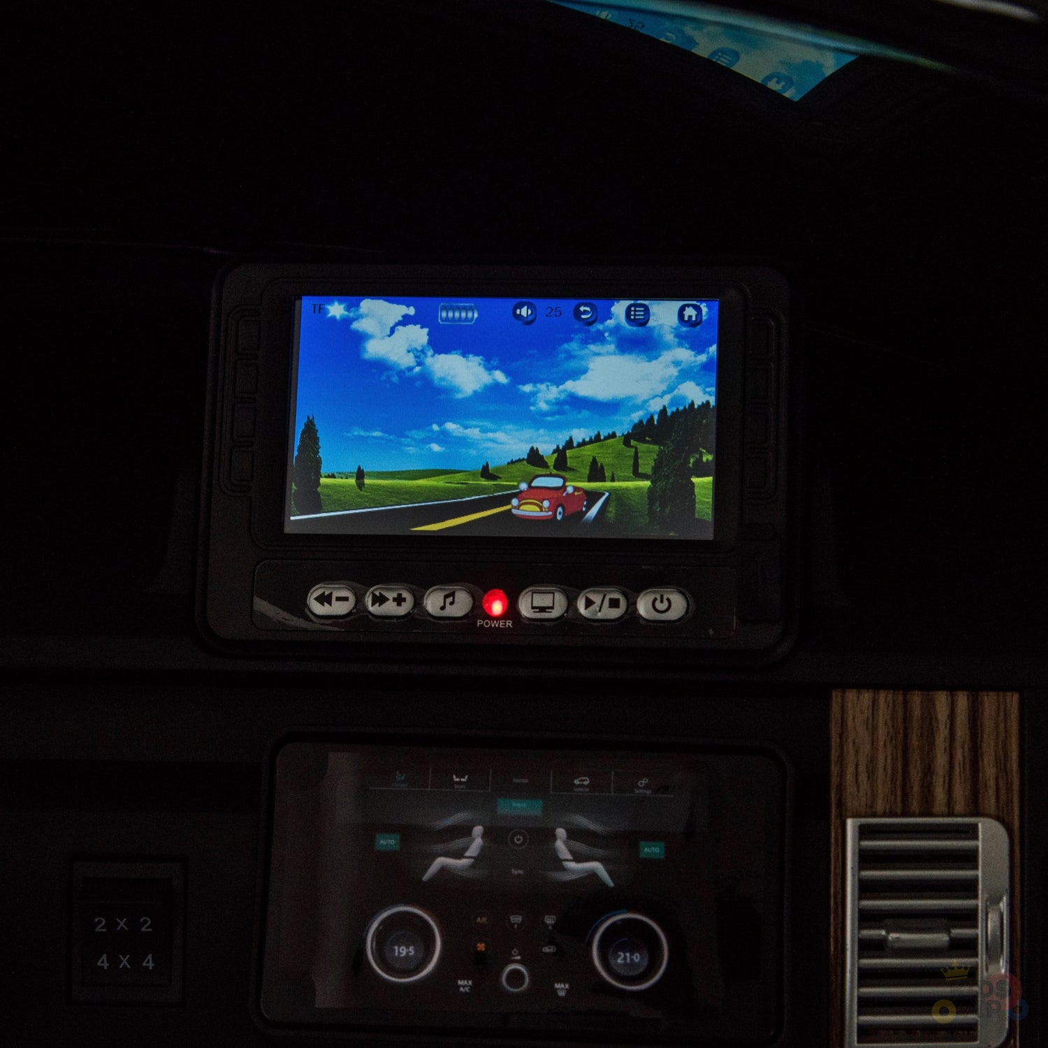 A Range Rover dashboard displays a driving simulation with a red car on a scenic, tree-lined, hilly road. Below, upgraded features on the control panel mirror those in the Black 24V Official Range Rover Complete MP4 Edition Kids Ride On Car with RC.