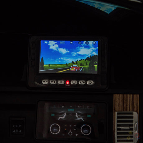 A Range Rover dashboard displays a driving simulation with a red car on a scenic, tree-lined, hilly road. Below, upgraded features on the control panel mirror those in the Black 24V Official Range Rover Complete MP4 Edition Kids Ride On Car with RC.