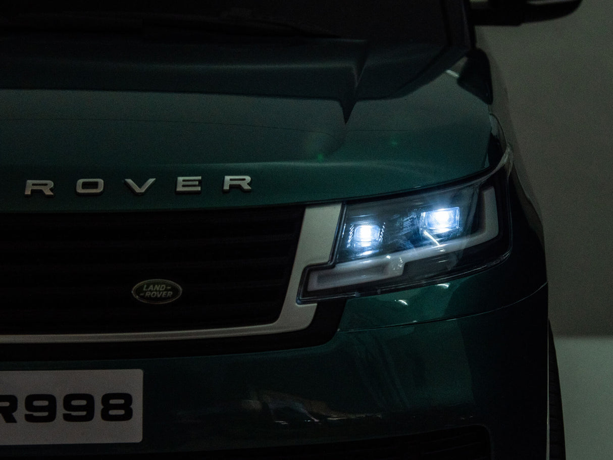 Close-up of the front of a Red Metallic 24V Range Rover Ride-On SUV with EVA Wheels & Parental Control, featuring illuminated headlights and a visible grille. The license plate reads R998, highlighting the sleek design and commanding presence on its front left side.