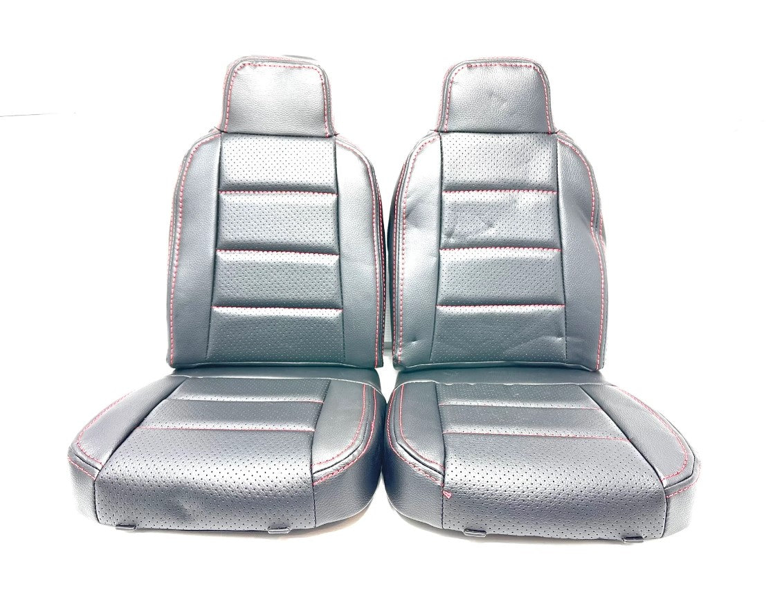 The 24V Audi Q5 Seats, with black upholstery and red stitching, feature a perforated texture for superior comfort. They have high backs, sitting cushions, visible horizontal seams, and are displayed side by side against a white background.