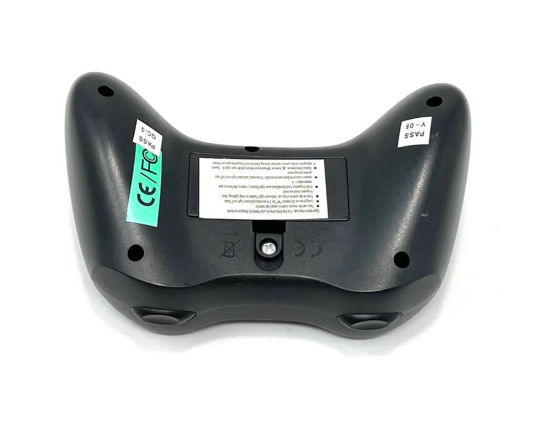 The New Remote for 24V Tundra XXL is a black video game controller with ergonomic grips, featuring two side trigger buttons, similar in precision to the ride-on car remote. It has labels including a green CE/FCC sticker and white text on the back view.