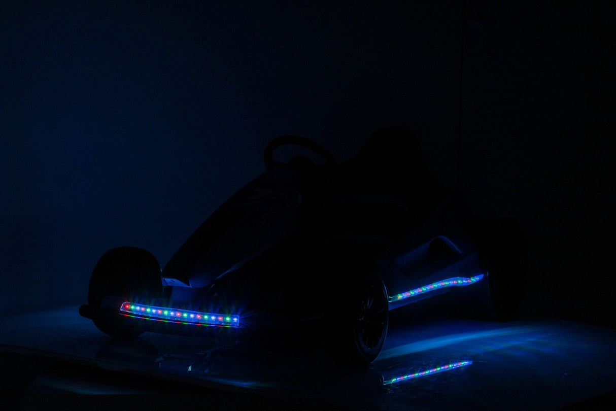 A Big Kids 24 Volt Ultra-Violent Complete Edition Drifting Go-Kart with colorful LED lights accentuating its front and sides is parked on a dark surface, with the dim backdrop enhancing its vibrant glow.