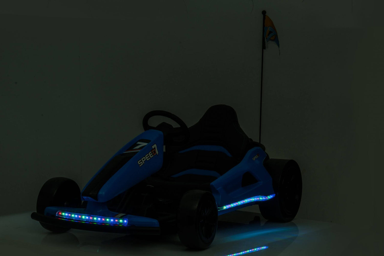 A Big Kids 24 Volt Ultra-Violent Complete Edition drifting go-kart in blue, parked indoors with LED lights along its sides and front. It boasts a steering wheel, seat, and rear flag for thrilling rides.