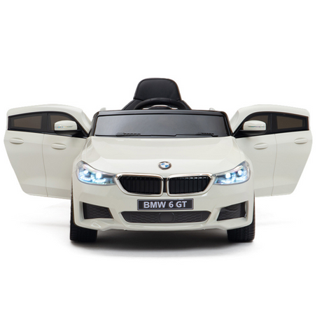 The White 12V BMW GT Kids Licensed 1 Seater Ride On Car, featuring rubber wheels and a remote, has openable doors that reveal black details on the grille, mirrors, and seating. With working headlights, it captures the charm of a BMW 6 GT from its front view.