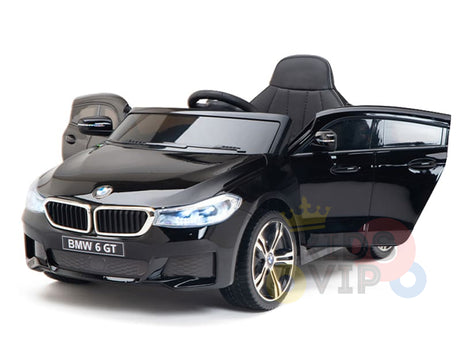 The Black Licensed BMW GT 12V Kids Ride On Power Car features upgraded chrome accents and detailed headlights. The model, styled with an open drivers side door, visible steering wheel, and seat, is set against a white background.