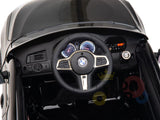 Close-up of a Black Licensed BMW GT 12V Kids Ride On Car dashboard with BMW logo on the steering wheel. Features include two circular gauges, a digital display on the right, buttons, and air vents on the left in this official electric ride-on.