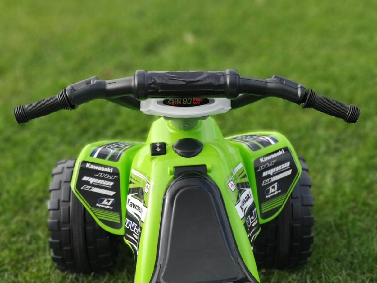 Close-up of the green INJUSA Official 12V Kawasaki Ride-On Quad for kids on grass, showcasing the handlebars, controls, sporty decals with brand logos and specs, ideal for off-road fun.