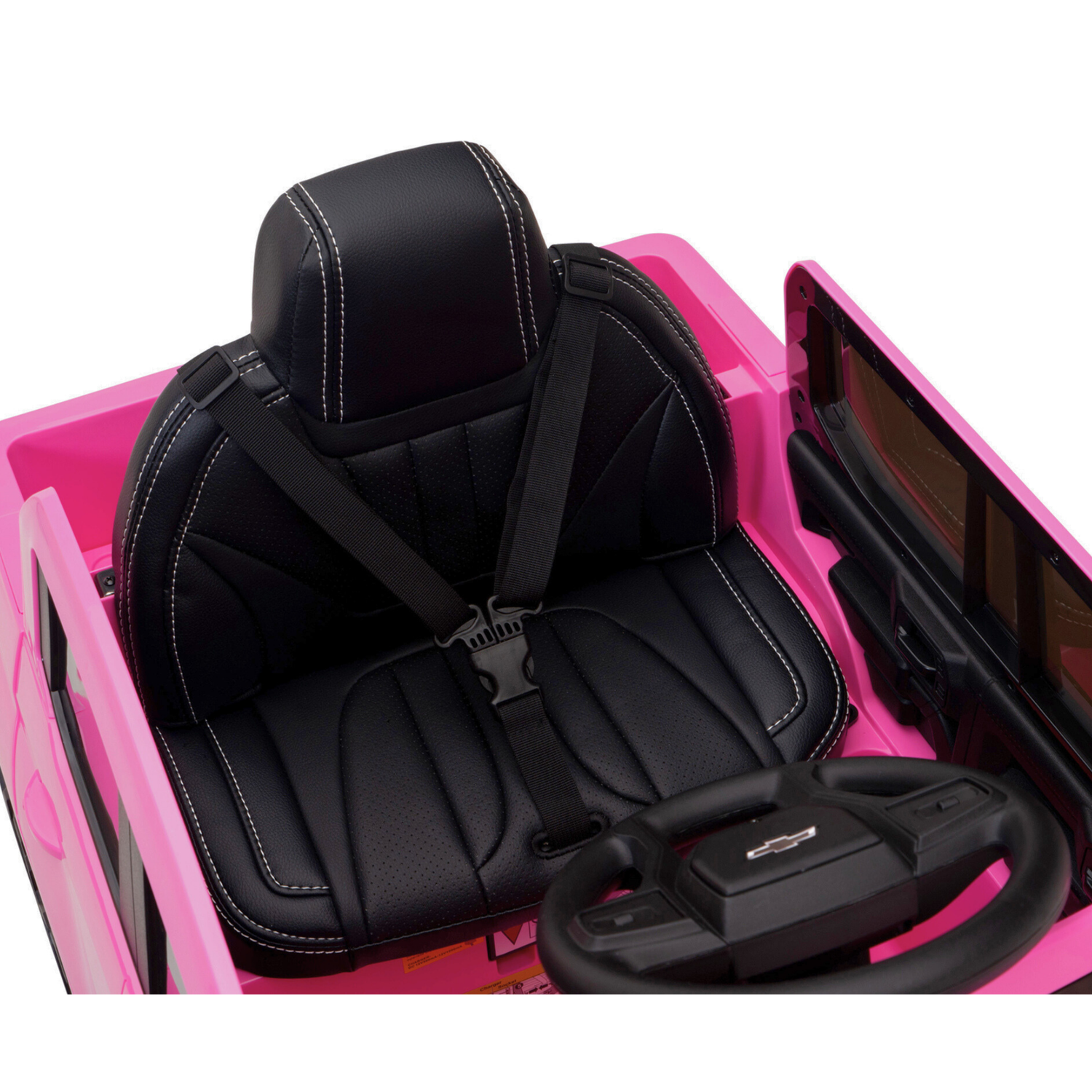 A close-up of the Pink 12V Chevrolet Silverado Ride-On Truck shows a black leather seat with white stitching, safety harness, logo-printed steering wheel, and windshield.