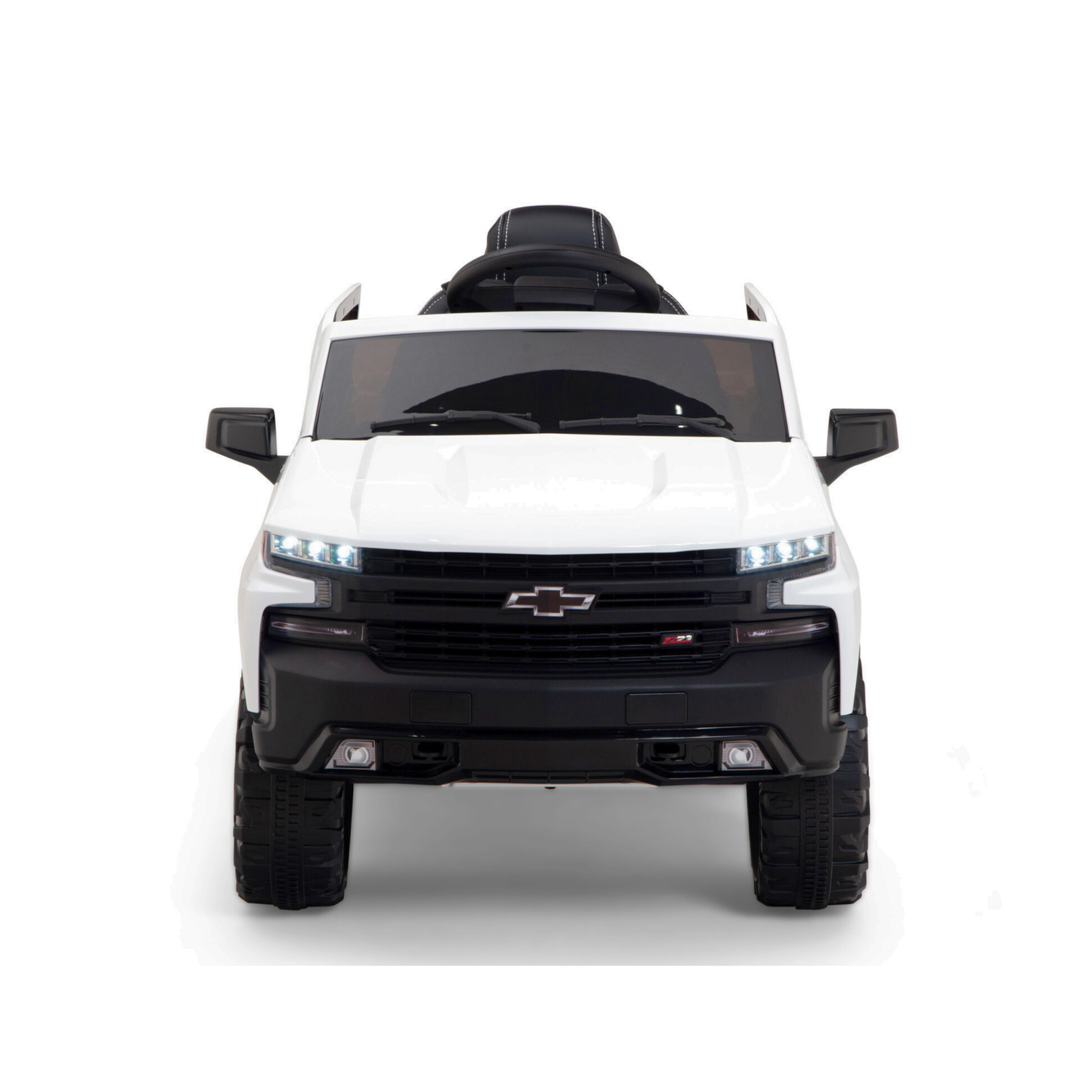 Front view of a white 12V Chevrolet Silverado ride-on truck for kids features upgraded elements like a realistic grille, LED lights, black accents, oversized wheels, and visible steering wheel. It includes music and remote control functionality.