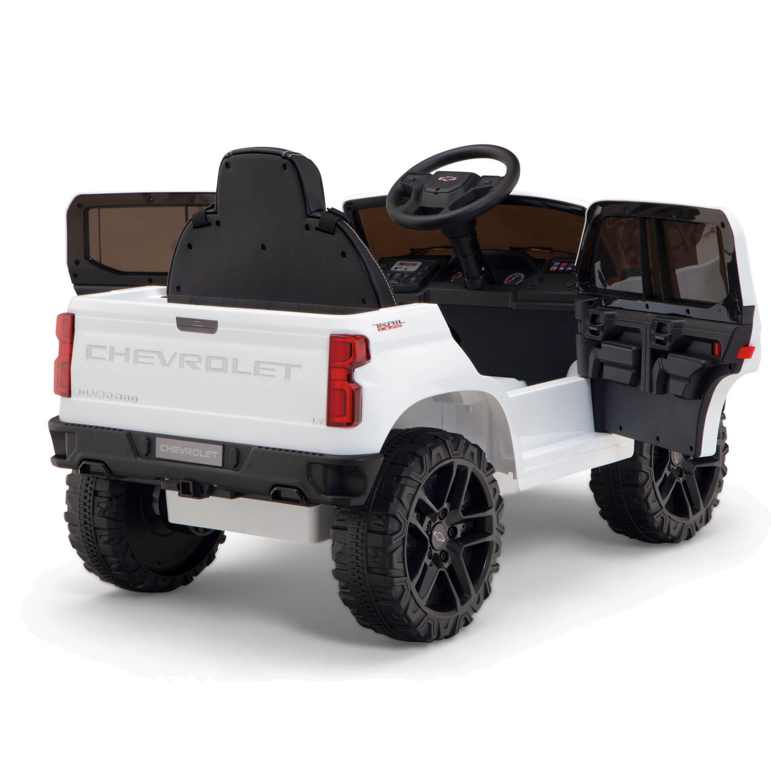 A rear-angle view of the White 12V Chevrolet Silverado Kids Licensed Ride On Truck showcases its large black wheels and open-back design. This 1-seater toy car features upgraded elements like a steering wheel, with the drivers door open to reveal the interior.