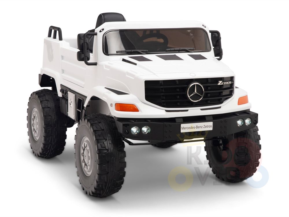 The White 12V Mercedes Benz Zetros Kids 1 Seater Ride On Truck features rubber wheels, a black seat, and front headlights. It showcases a large emblem on the grille, resembling an off-road vehicle for adventurous little drivers.