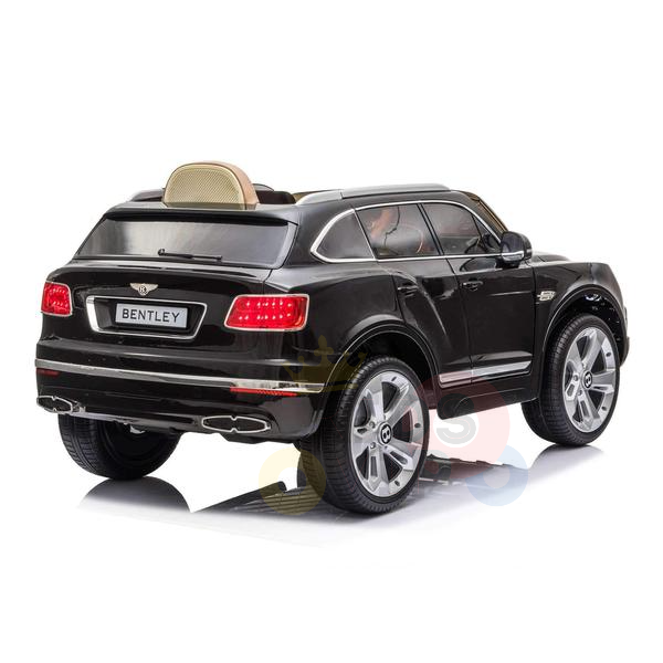 A stylish Black Licensed Bentley Bentayga 12V Kids Ride On Car, captured from the back right angle, features glossy paint, silver wheels, a miniature license plate, and a tan leather seat. Set against a white backdrop, it also includes a parental remote for enhanced safety.