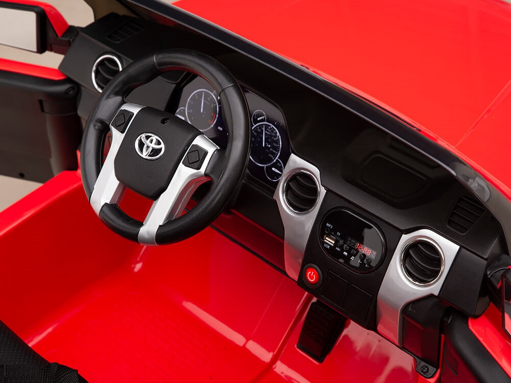 The interior of the Red 12v Licensed Toyota Tundra, a 2-seater kids ride on truck, features a red dashboard and seating. It includes a Toyota-emblazoned steering wheel, detailed speedometers, and a central control panel with buttons and knobs—ideal for two adventurous young riders.