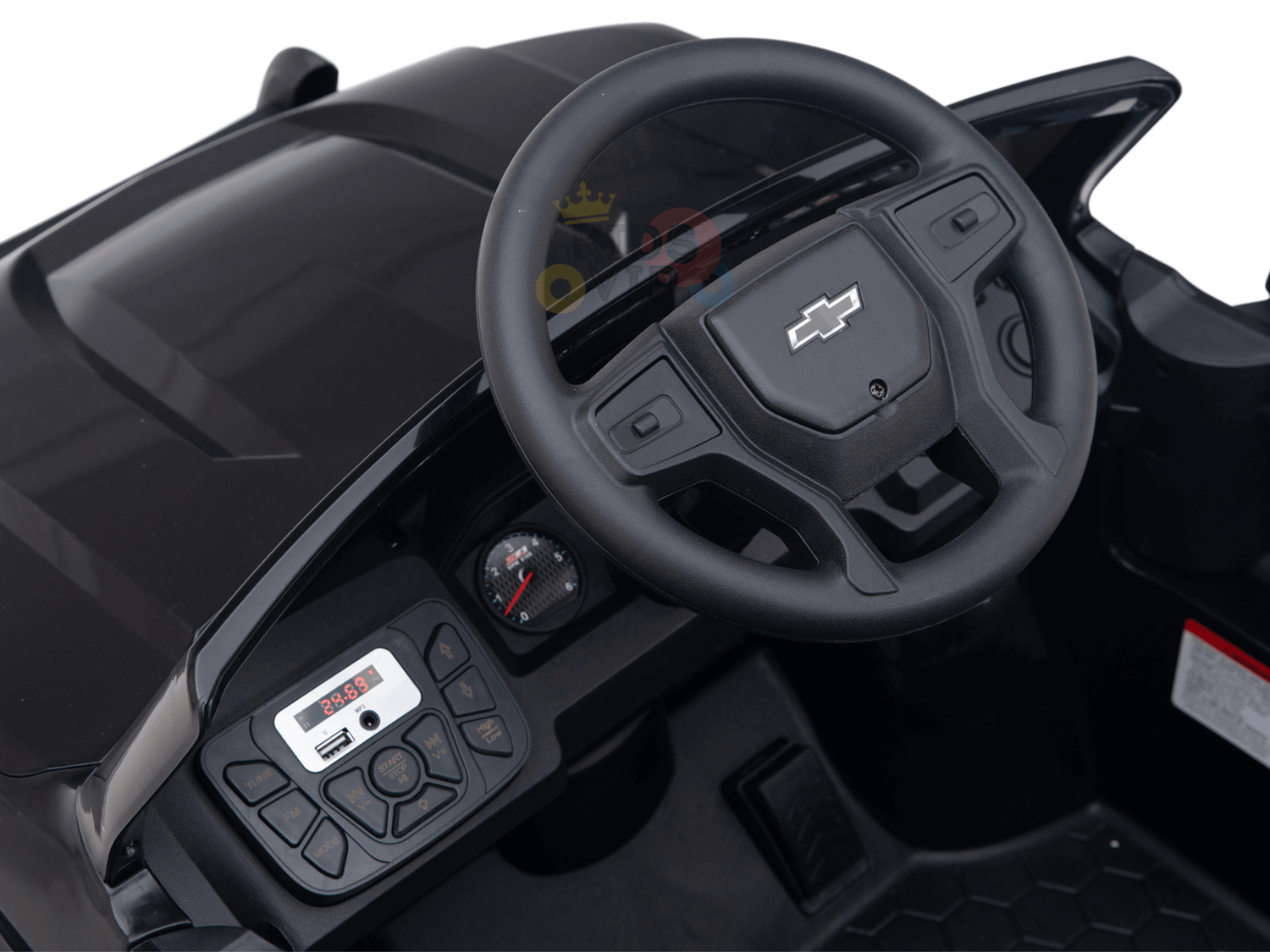 Close-up of a black toy cars interior, resembling the Black Official 24V Chevrolet Silverado Lifted Kids Ride-on Truck. It features an iconic logo on the steering wheel and a dashboard with a speedometer and control buttons on a textured surface.