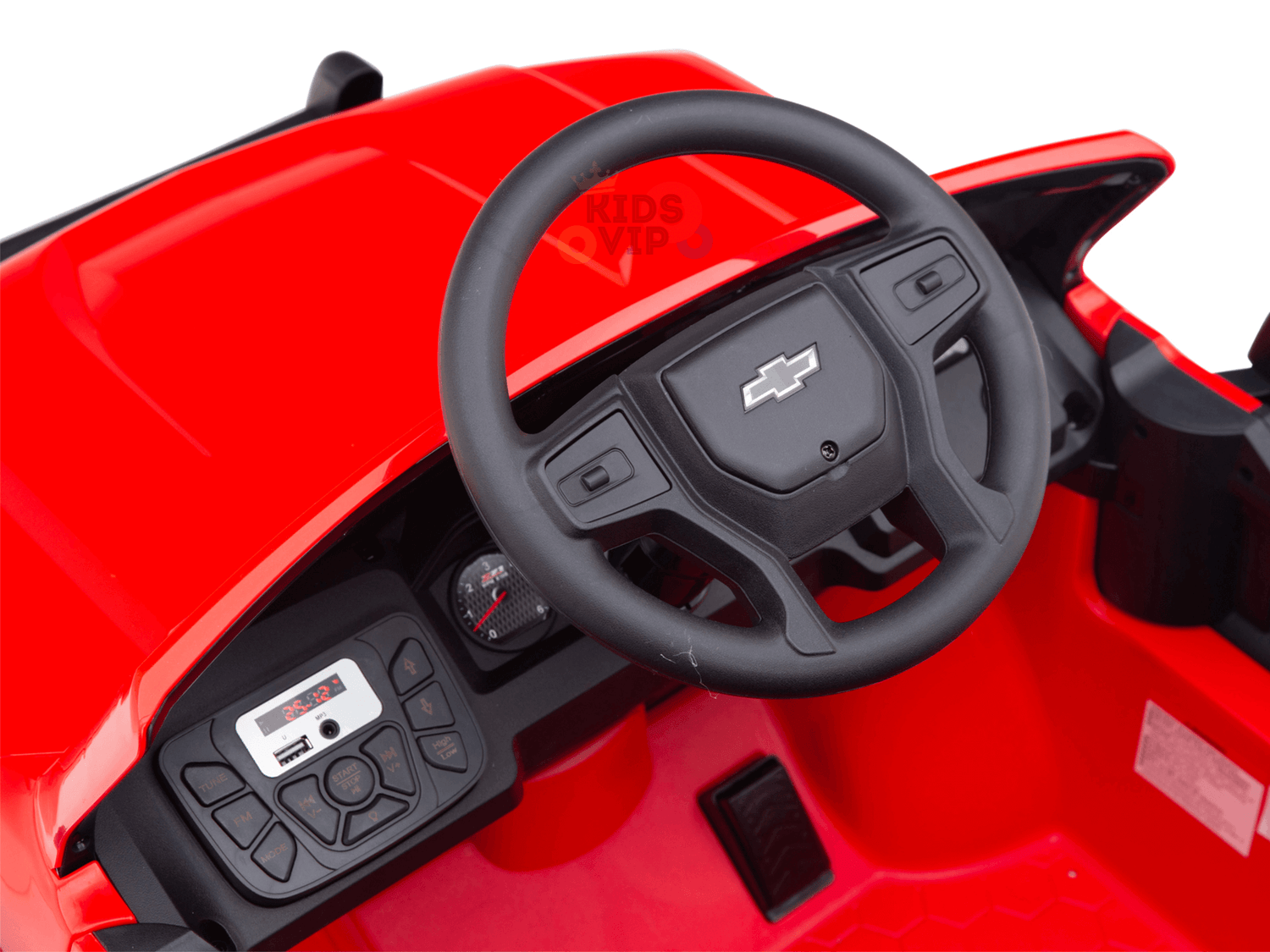 Close-up of a red toy cars interior from the Red 24V Chevrolet Silverado Kids Licensed 1 Seater Ride On Lifted Truck, featuring a black steering wheel with a Chevrolet logo, dashboard with speedometer and stereo-like panel, and a stylish hexagonal patterned floor for mini adventures.