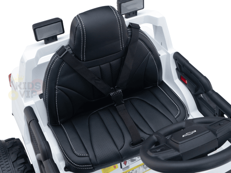 A close-up of the white Chevrolet Silverado Kids 24V ride-on trucks black leather seat with white stitching exudes its rugged charm. The seat features a safety harness, and the dashboard with simple controls along with the steering wheel is visible.