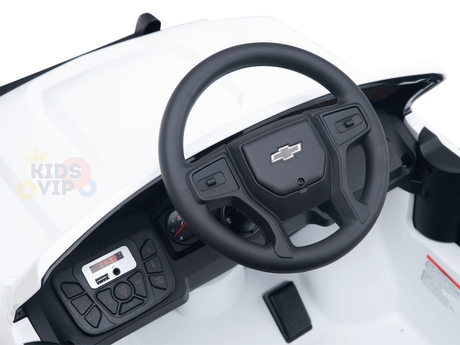 A close-up of the White 24V Chevrolet Silverado Kids Licensed 1 Seater Ride On Lifted Truck dashboard reveals a black Chevrolet-logo steering wheel, intricate control panel, and digital display. The interior features realistic detailing, with a primarily white design accented in black.