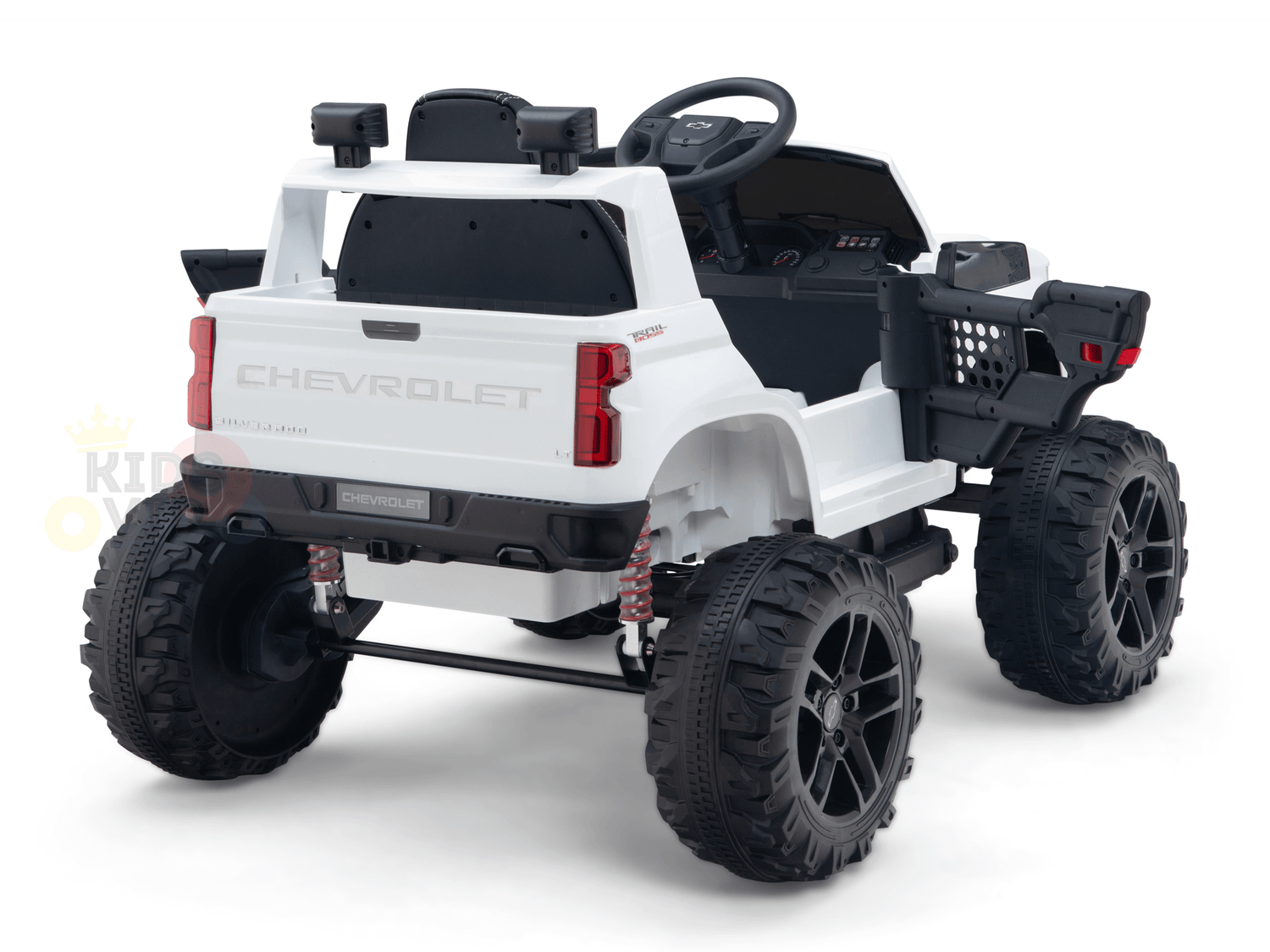 The rear angle of the White 24V Chevrolet Silverado Kids Licensed 1 Seater Ride On Lifted Truck with Remote shows oversized black tires, a detailed dashboard, and realistic elements like a tailgate and side mirrors. The toy is set against a white background.