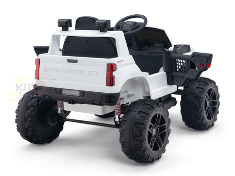 The rear angle of the White 24V Chevrolet Silverado Kids Licensed 1 Seater Ride On Lifted Truck with Remote shows oversized black tires, a detailed dashboard, and realistic elements like a tailgate and side mirrors. The toy is set against a white background.