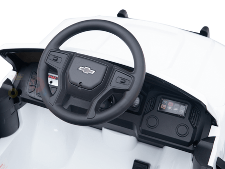 In the White 24V Chevrolet Silverado Ride-On Truck, the miniature dashboard showcases detailed controls and screen displays within a white interior, highlighting a black steering wheel with the Chevy logo—capturing the true essence of this kids licensed product.