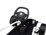 Close-up of the 24V Sport Challengers steering wheel, showcasing a black circular design with buttons. The drifting kart features a sleek black seat, white frame, visible pedals, front wheels on a black platform, and a colorful crown-like logo below the seating area.