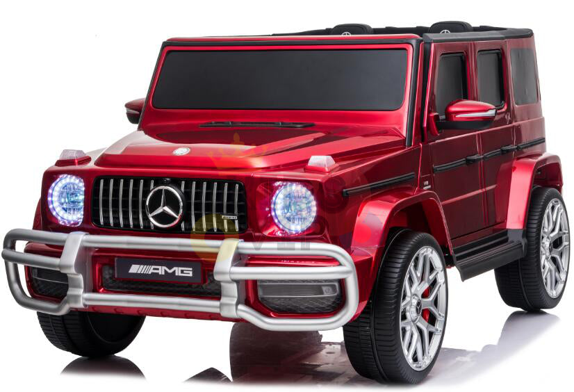 The 2 Seats 4x4 Official Mercedes Benz G63 Complete Edition Red 24V Kids Ride On Car with RC showcases detailed elements, bright headlights, and AMG branding. Viewed from a front-side angle, the ride-on highlights its robust tires and sleek design.
